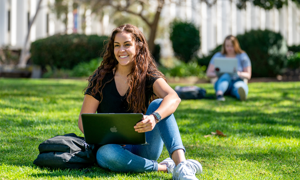 sdsu student sitting on grass, with laptop